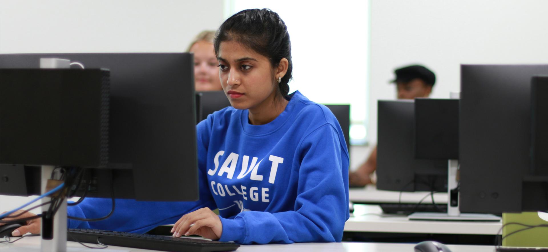 Student sitting at computer in class wearing blue ϲͼȫ sweater
